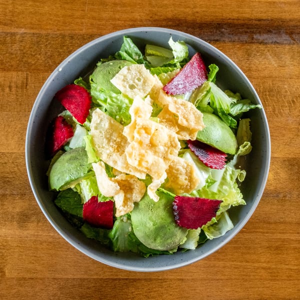 Overhead view of a vibrant salad with lettuce, avocado, red beets, and crispy wonton strips.
