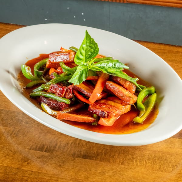 Crispy pork belly with green beans, red peppers, and basil in a rich sauce.