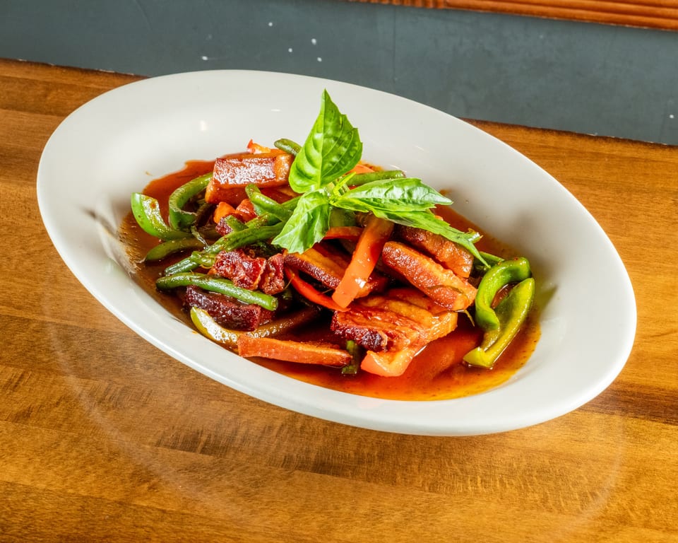 Crispy pork belly with green beans, red peppers, and basil in a rich sauce.