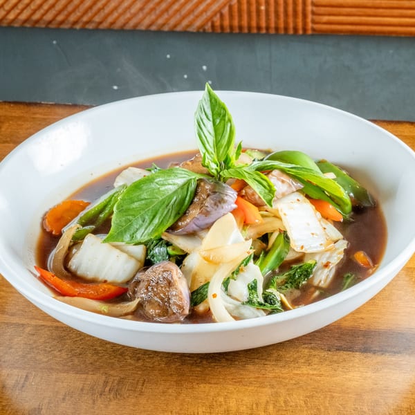 Steaming bowl of colorful stir-fried vegetables in a rich brown sauce, garnished with fresh basil.