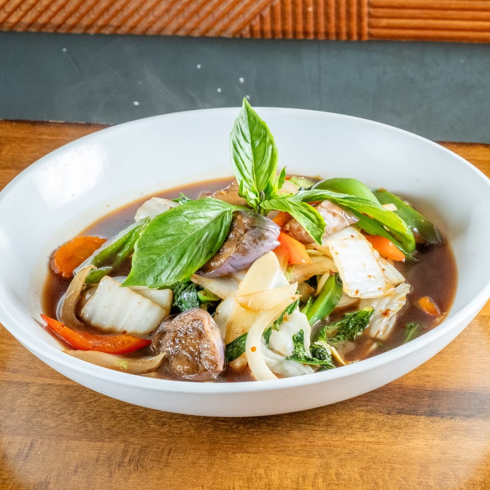 Steaming bowl of colorful stir-fried vegetables in a rich brown sauce, garnished with fresh basil.