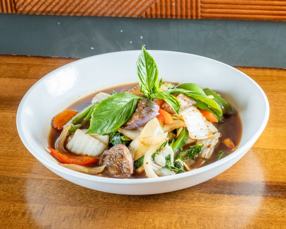Steaming bowl of colorful stir-fried vegetables in a rich brown sauce, garnished with fresh basil.