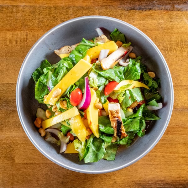 Overhead view of a vibrant salad with grilled chicken, mango, lettuce, tomatoes, and red onion.