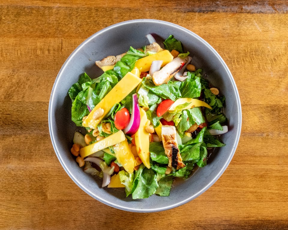Overhead view of a vibrant salad with grilled chicken, mango, lettuce, tomatoes, and red onion.