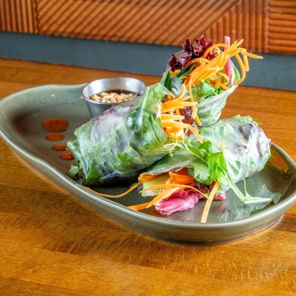 Two fresh spring rolls filled with greens and carrots, served with peanut sauce on a green plate.