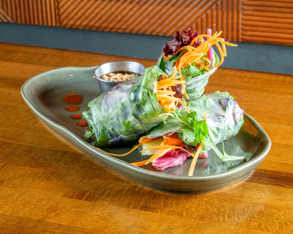 Two fresh spring rolls filled with greens and carrots, served with peanut sauce on a green plate.