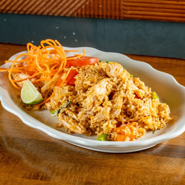 Chicken fried rice with shredded carrots, tomato slices, and a lime wedge on a white plate.