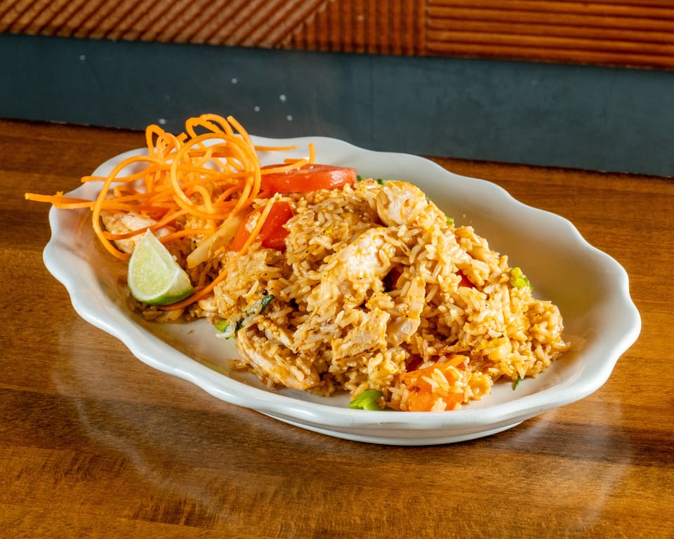 Chicken fried rice with shredded carrots, tomato slices, and a lime wedge on a white plate.