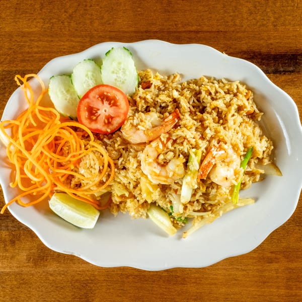 Shrimp fried rice with shredded carrots, cucumber slices, tomato, and a lime wedge on a white plate.