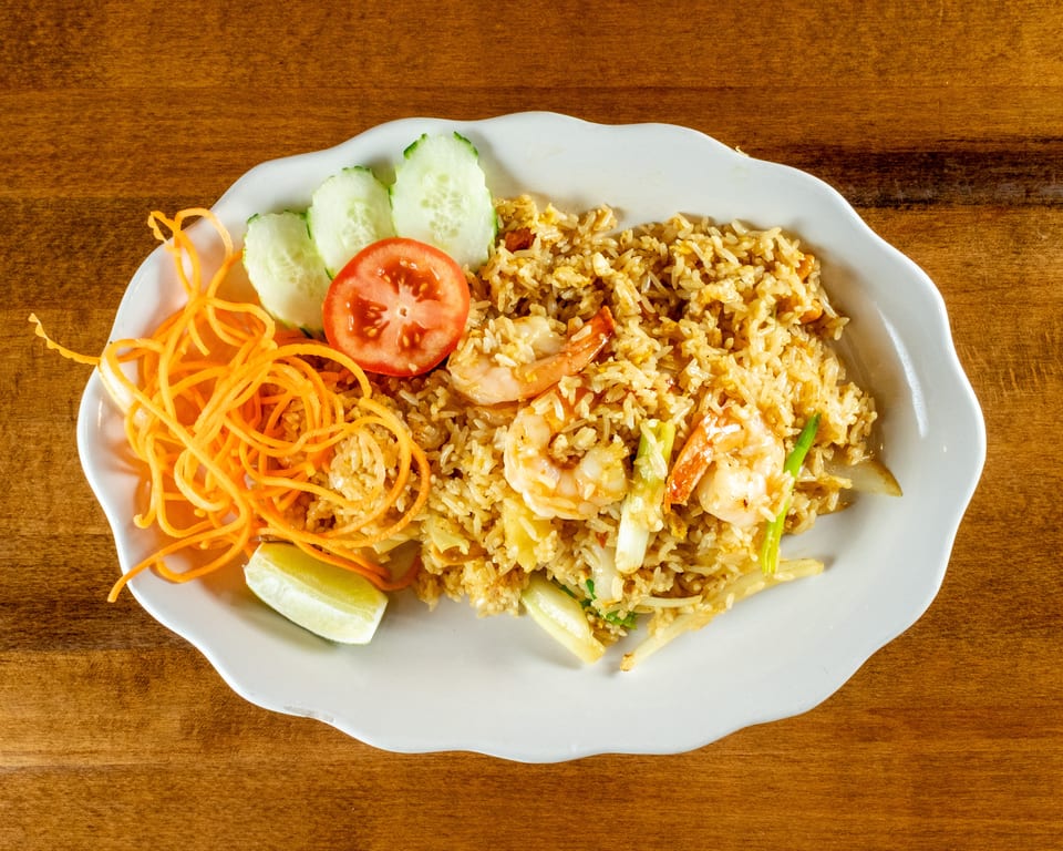 Shrimp fried rice with shredded carrots, cucumber slices, tomato, and a lime wedge on a white plate.