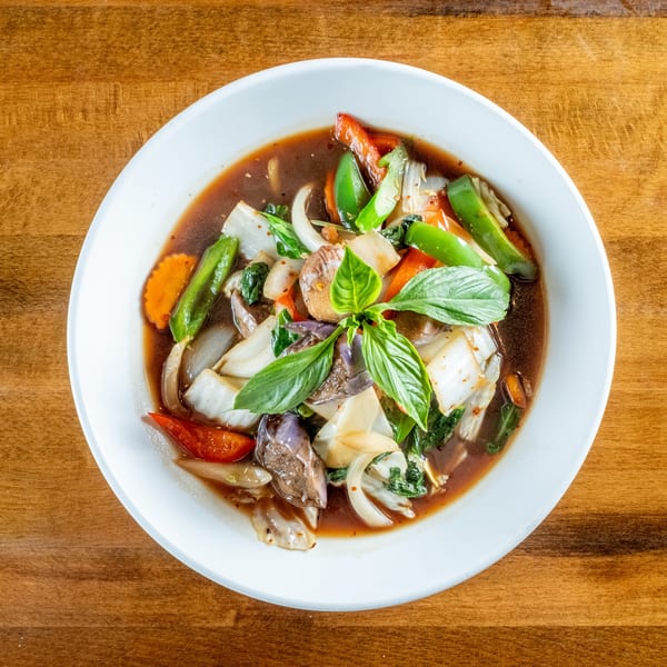 Overhead view of a white bowl filled with stir-fried vegetables in a dark sauce, garnished with basil.