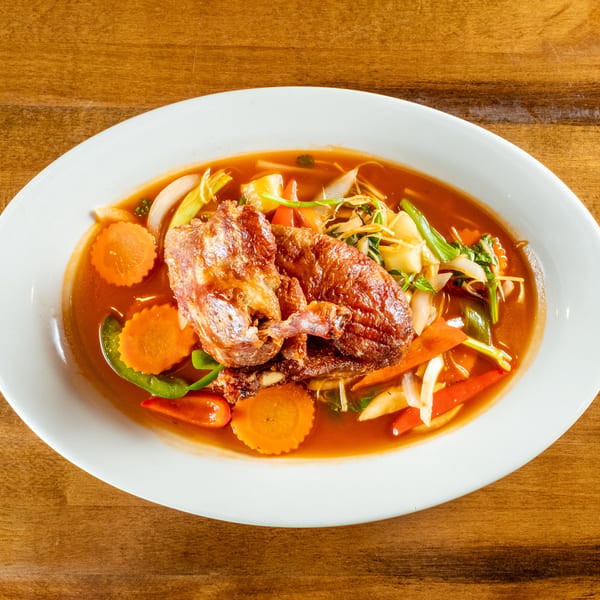 Crispy duck in red curry sauce with carrots, bell peppers, and onions on a white plate.