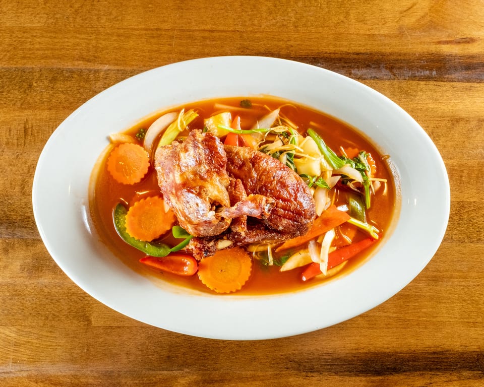 Crispy duck in red curry sauce with carrots, bell peppers, and onions on a white plate.