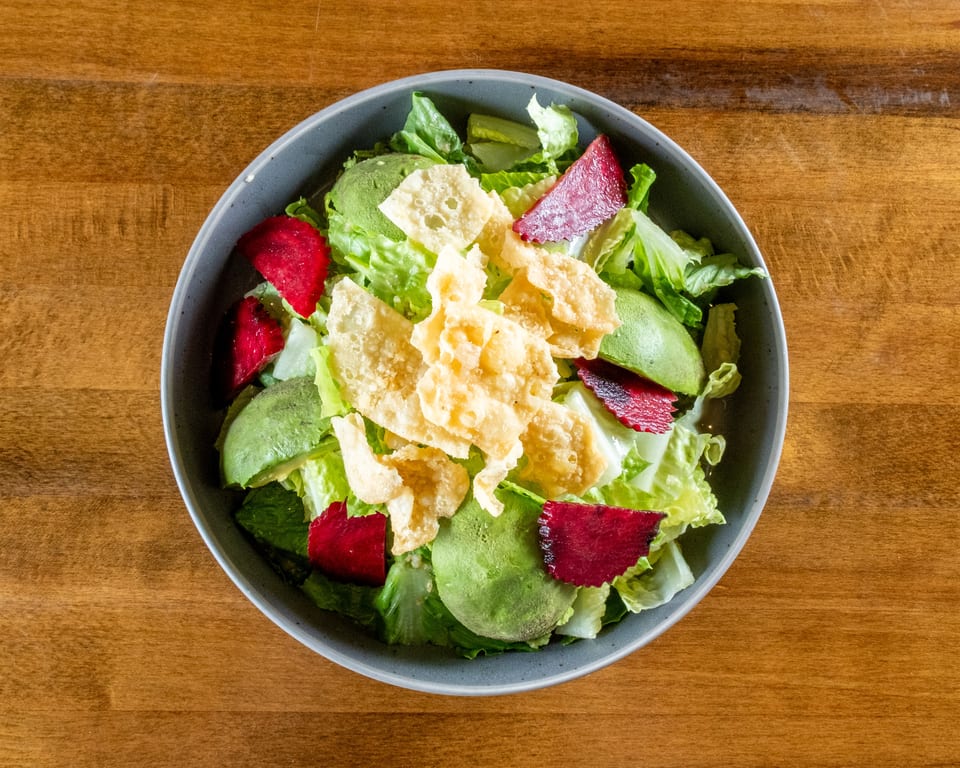 Overhead view of a vibrant salad with lettuce, avocado, red beets, and crispy wonton strips.