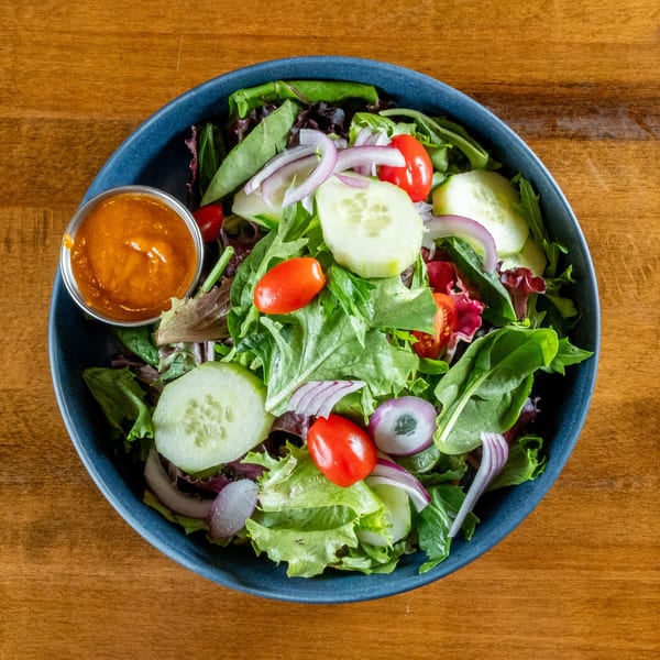 Fresh garden salad with mixed greens, cherry tomatoes, cucumbers, red onions, and a side of dressing.
