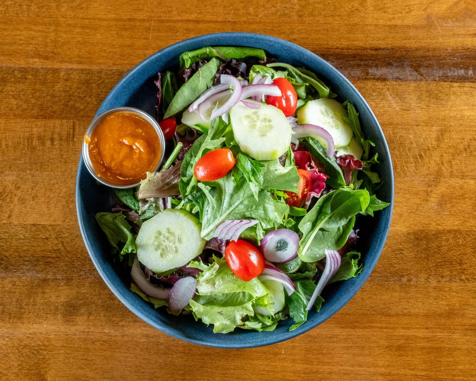 Fresh garden salad with mixed greens, cherry tomatoes, cucumbers, red onions, and a side of dressing.