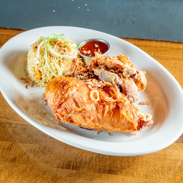 Crispy fried chicken, fried rice, and a side of red sauce on a white plate.