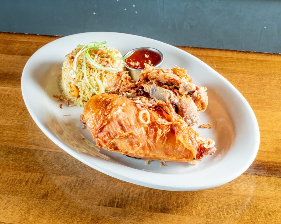 Crispy fried chicken, fried rice, and a side of red sauce on a white plate.