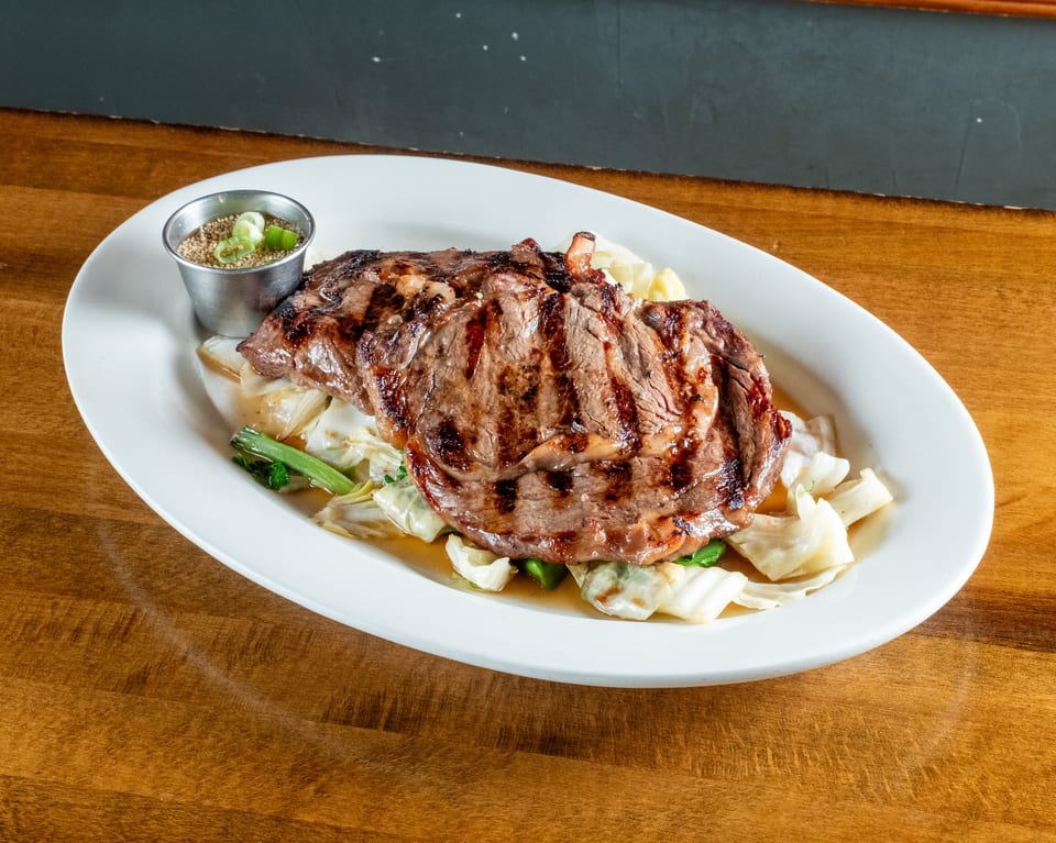 Grilled steak with grill marks, served over cabbage and bok choy, with a side of sauce.