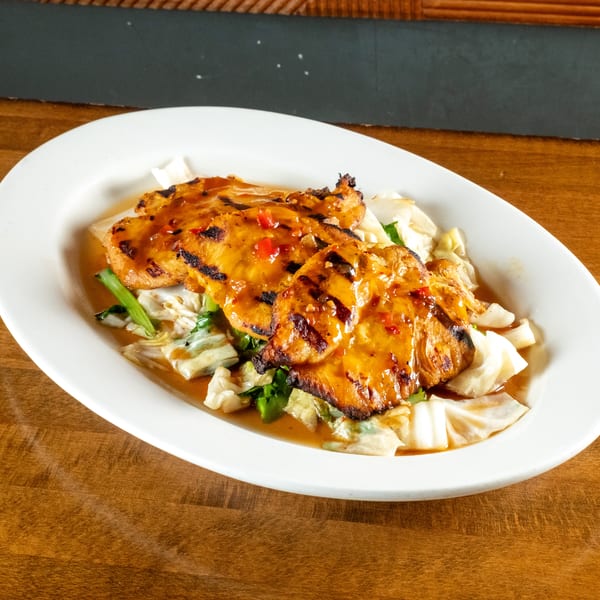 Grilled chicken with chili sauce and cabbage on a white oval plate, on a wooden table.