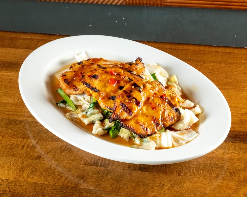 Grilled chicken with chili sauce and cabbage on a white oval plate, on a wooden table.